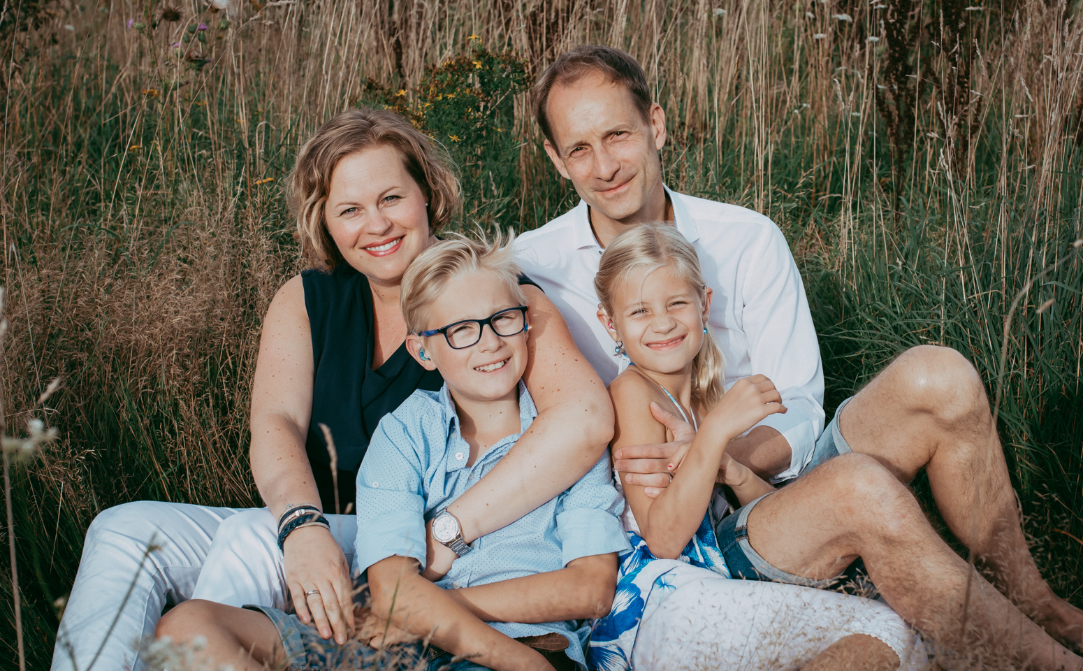 Familie sitzt im hohen Gras zusammen und lacht